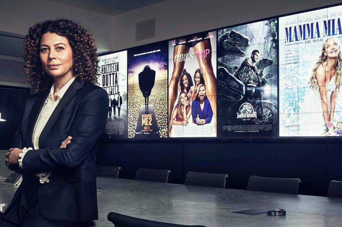 Universal Filmed Entertainment Group (UFEG) Chairman Donna Langley leans against a conference table in front of Universal Pictures posters, Straight Outta Compton, Despicable Me 2, Girls Trip, Jurassic World and Mamma Mia. 